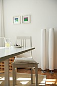 Two modern standard lamps against white wall in sunny kitchen; simple dining table and vintage chair with seat cushion in foreground