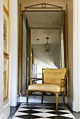 Upholstered chair in front of mirror with gold frame on checkered floor in transition