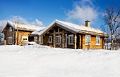 Wooden houses in snowy landscape below blue sky