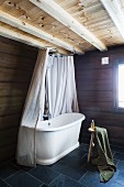 Vintage bathtub with shower curtain in corner of bathroom with grey tiled floor in rustic, modern interior