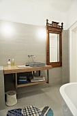 Modern washstand next to wall-mounted mirror with antique wooden frame in designer bathroom