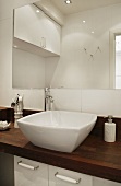 Designer washstand with basin on dark wood counter in front of simple wall-mounted mirror