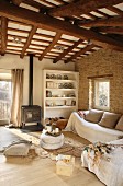 Comfortable couch behind stacked pouffes in rustic living room with wood-burning stove below wood-beamed ceiling