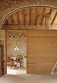 Wooden partition in hall-like interior of converted, Mediterranean country house; view of dining area in background