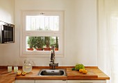 Kitchen counter with wooden counter top and built in sink in front of a window and a view of herbs in plant pots