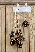 Pine cones hanging on festive ribbons from hooks on wooden wall