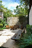 Bench carved from natural tree trunk and seating area in sheltered courtyard with high stone walls