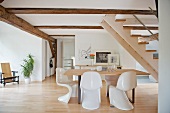 Essplatz unter Treppe mit Schalenstühlen aus weißem Kunststoff in offenem Wohnraum mit sichtbarer Holzkonstruktion an Wand und Decke