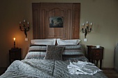 Eclectic bedroom with bedspread in modern tones of grey on double bed combined with wood panelling flanked by antique sconce lamps and Rococo bedside cabinets