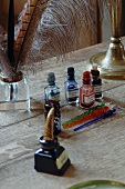 Fläschchen mit verschiedenfarbigen Tinten und Federkiele auf altem Schreibtisch