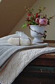 Wellness im romantischen Naturlook - Seifenpäckchen auf Handtuch und Spitzenbordüre, im Hintergrund Rose in Porzellanbecher
