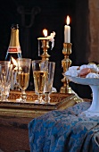 Gefüllte Sektgläser auf Tablett vor Messing-Kerzenständern mit brennenden Kerzen und Porzellanschale mit Konfekt auf Tischtuch