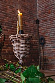 Lit candle in metal and wicker candlestick on table in front of interior corner with exposed brick walls