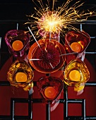 Top view of still-life with glass tealight holders in various shades of red and sparkler on black metal lattice