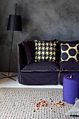 Scatter cushions on sofa with indigo upholstery and black standard lamp against dark grey wall