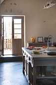 Traditional kitchen island with sink and designer tap fittings in front of half-open, double terrace door in simple, country-house kitchen-dining room