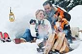 Couple sitting next to camp fire in snow