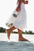 Girl on beach carrying jar of shells