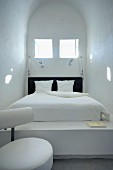 Gemauertes Bett unter quadratischen Fenstern in einem schmalem Raum mit Tonnendach