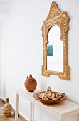 Moroccan mirror above clay pot and collection of seashells on console table