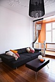 Retro coffee table with black leather cover and modern sofa on wooden floor in front of apricot window bay with platform