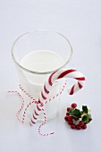 Candy cane tied to glass of milk next to holly berries