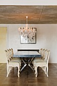 Table and vintage-style, pale chairs below chandelier hanging from exposed concrete ceiling