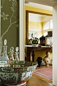 Valuable china bowl and crystal decanters next to open door with view of ornaments on console table