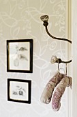 Padded coat hangers on antique hook with glass knobs; framed drawings on wallpapered wall