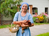 Bäuerin hält Korb mit frischen Eiern und lebendiges Huhn