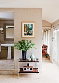 Bouquet on console table below modern painting on wall with natural fibre wallpaper next to open bathroom door