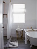 White-tiled bathroom with concrete floor, antique bathtub and shower area screened by shower curtain