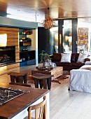 Open-plan interior in shades of brown with dining table, fitted cabinets with integrated fireplace, couch & African wooden stools