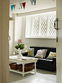 Seating area with black leather sofa below latticed window, vase of flowers on table and colourful bunting