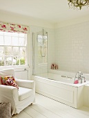 Helles Badezimmer mit Badewanne, weißem Polsterstuhl und weißem Holzboden