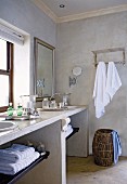 Stone washstand with twin basins, laundry basket and towels hanging on wall in bathroom