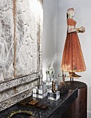 Chinese puppet of woman on pedestal and collection of statues on plexiglass plinths in front of stone relief on stone surface