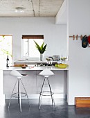Bar stools at counter in bright, open-plan fitted kitchen without wall units