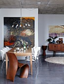 Dining table, designer chairs and wire lamp in front of large painting in open-plan interior