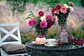 A garden table laid with Bundt cake, teacup, summer flowers and a hurricane lamp