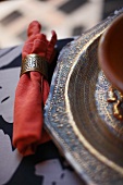 Red napkin with brass napkin ring next to chased metal tray