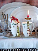 Becher mit Weihnachtsdeko auf Silberschale vor Gläsern und weissen Porzellanschalen