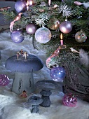 Weihnachtskugeln und brennende Kerzen am Baum neben Pilzfiguren auf Tierfell am Boden