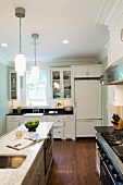 White country-house kitchen with island below traditional pendant lamps