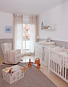 Elegantes Kinderzimmer mit gepolstertem Schaukelstuhl, Gitterbettchen und Wickelkommode im traditionellen Landhausstil