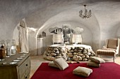 Vaulted room with antique armchair and cushions on red rug in front of twin bathtubs with surround made of boulders