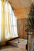 Rustic shower area in corner next to window with airy curtain and barrel vaulted ceiling