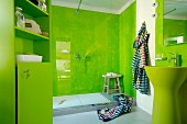 Designerbad mit grün marmorierten Wandflächen hinter Waschbecken und Duschbereich mit Glasabtrennung