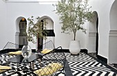 Table and wire shell chairs on black and white tiled floor with zigzag pattern in Moroccan courtyard