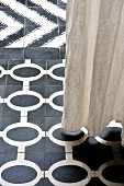 Floor-length linen curtain above different styles of black and white floor tiles with graphic patterns